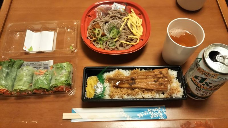 Anago rice, soba noodles, fresh spring rolls, and canned beer in a hotel room